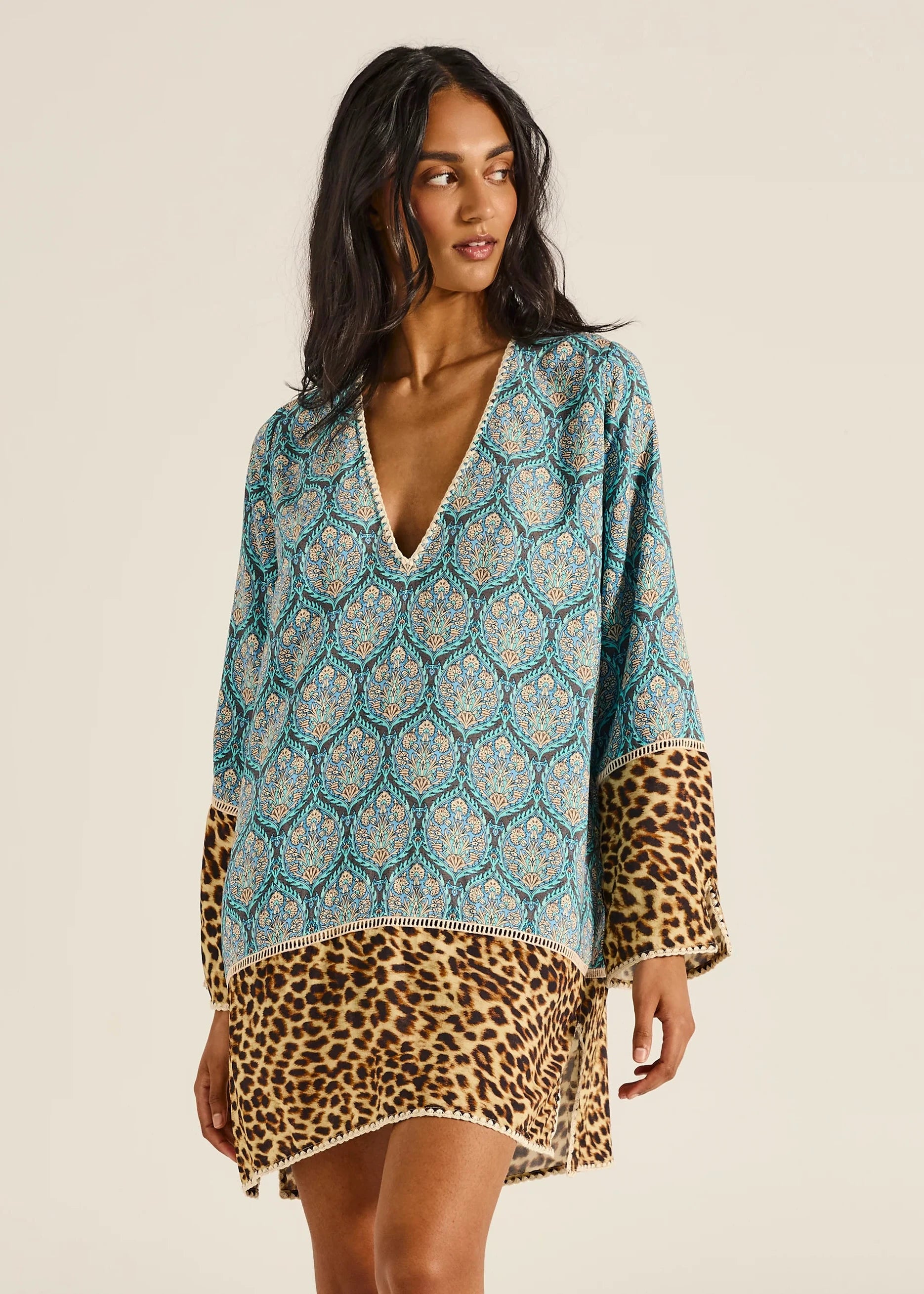 Woman wearing a patterned top with leopard print trim on a beige background
